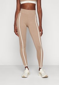 Bä beige leggings med vita sidostråkar, hög midja, stretchigt tyg och en slät textur, kombinerat med ljusa träningsskor.