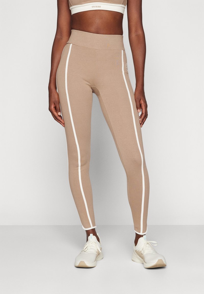 Bä beige leggings med vita sidostråkar, hög midja, stretchigt tyg och en slät textur, kombinerat med ljusa träningsskor.