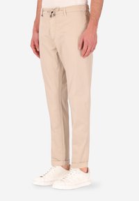 Pantaloni in misto cotone beige con vita regolabile, vestibilità affusolata e orli arrotolati, abbinati a sneaker bianche.