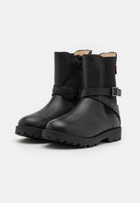 Botas de cuero negras hasta el tobillo con un acabado texturizado, que cuentan con un zipper lateral, una correa para el tobillo con hebilla y suelas de goma resistentes.