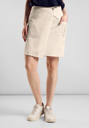 Beige omlottkjol i lättviktig tyg, med två sidofickor, knäppning med knapp och en ren fåll, i kombination med vita sneakers.