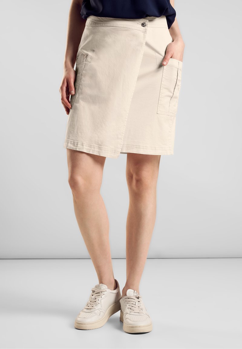 Beige wikkelrok van lichtgewicht stof, met twee zijzakken, een knoopsluiting en een nette zoom, gecombineerd met witte sneakers.