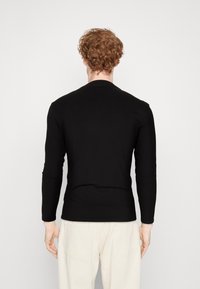 Zwarte langek mouwen shirt met een ronde hals, strakke pasvorm en gladde textuur, getoond vanuit de rug, gecombineerd met lichtgekleurde broeken.