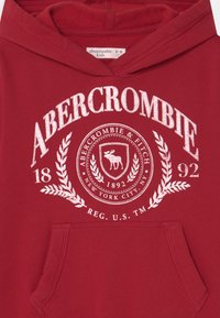 Hoodie rouge avec une poche avant, un texte graphique blanc et un emblème, et une texture douce. L'étiquette indique une taille 9/10 de chez Abercrombie Kids.