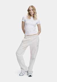Valkoinen istuva t-paita yhdistettynä vaaleanharmaisiin, joustovyötäröisiin collegehousuihin, joissa on sivutaskut ja logo. Malli seisoo lenkkareissa.