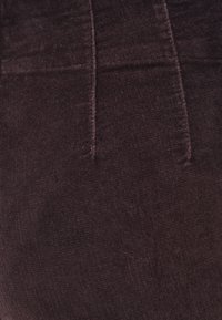 Ciemnobrązowy materiał z korduroju o miękkiej, teksturowanej powierzchni z pionowymi żeberkami oraz starannym przeszyciem wzdłuż pasa i szwów.