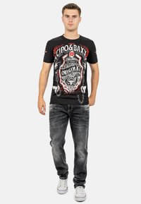 T-shirt grafico nera con disegni rosso e bianco, che mostra una tigre e del testo, abbinata a jeans grigi sbiaditi e sneakers bianche.
