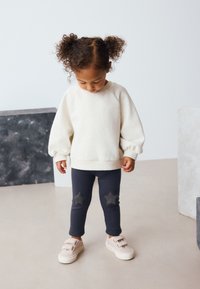 Sudadera de forro polar color blanco roto con mangas abullonadas; mallas azul marino con parches de estrellas grises; zapatillas con velcro rosa pálido.