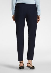 Pantaloni su misura blu navy con una texture liscia, vestibilità slim e due tasche posteriori, abbinati a tacchi aperti neri.