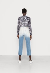 Blusa de mangas longas em padrão de leopardo preto e branco combinada com calças de ganga em degradê azul claro, com bainha desfiada e bolsos traseiros.