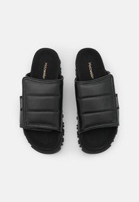 Paire de sandales slides noires avec larges brides rembourrées et semelles en caoutchouc, avec le logo "Holzweiler" sur les brides et les semelles intérieures.