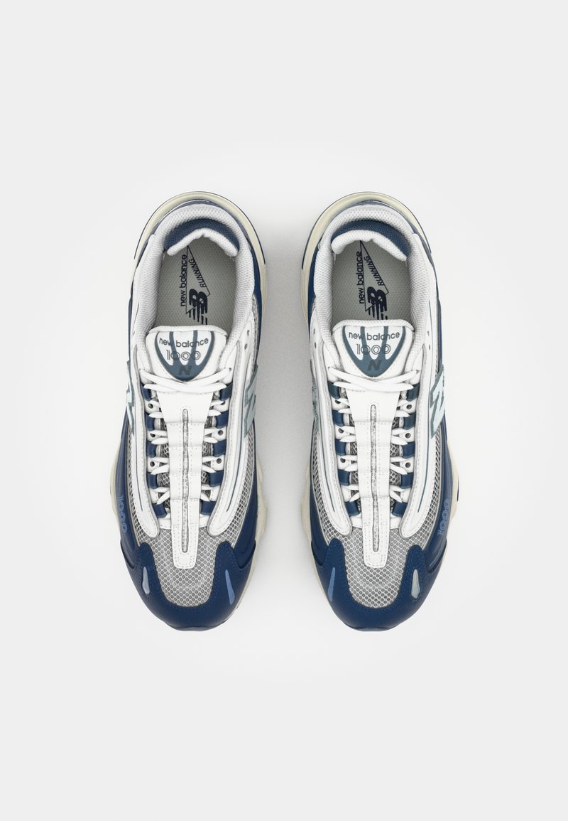 Las zapatillas blancas y marinas presentan una parte superior de tejido de malla, acentos de cuero en contraste y cordones. La suela tiene un diseño texturizado y redondeado.