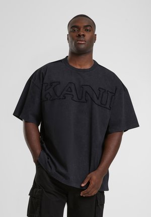 Svart oversized t-shirt med texturerad "KANI"-tryck på framsidan, rund halsringning och korta ärmar, tillverkad av ett mjukt, matt tyg.