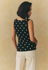 Black sleeveless top with white polka dots, fitted design. The model is paired with light-colored wide-legged pants.
