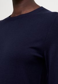 Maglione a maglia blu navy con scollo rotondo e maniche inserite. Texture liscia e cuciture minime visibili nella zona delle braccia.