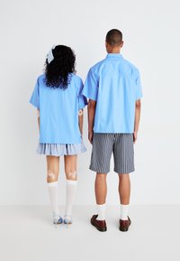 Lyseblå kortermede skjorter, litt overstore. Den kvinnelige modellen har på seg et blått rutete skjørt med volanger; den mannlige modellen har på seg stripete shorts.