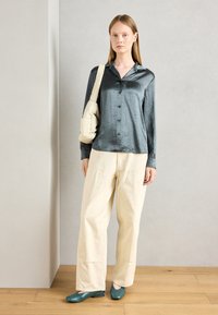 Camisa botonê de seda cinza escuro, calças largas creme e sapatilhas verdes. Detalhes da bolsa crossbody bege são notáveis. Design simples e moderno.