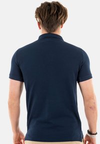 Polo blu navy con colletto e maniche corte, con polsini a coste e orlo dritto, realizzato in un tessuto liscio e resistente.
