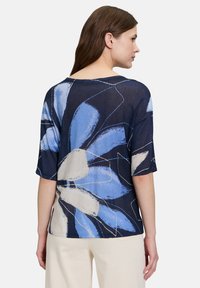 Granatowa bluzka z kwiatowym wzorem w odcieniach niebieskiego i kremowego, krótki rękawek, luźny krój, szeroki dekolt oraz miękka tekstura.