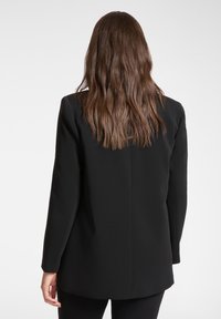 Blazer nero con design strutturato, maniche lunghe e tessuto liscio. Presenta una singola spacco posteriore e uno stile minimalista.