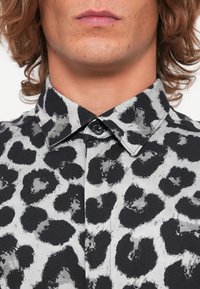 Sort og grå leopardmønstret skjorte med knapp-ned krage, med en glat tekstur og sorte knapper på placket.