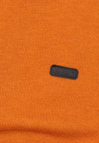 Oranje gebreid stof met een gladde textuur, voorzien van een zwart rechthoekig logo-label met de tekst "J&Joy" dat in de stof is genaaid.