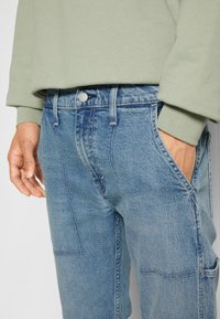 Světle modré džíny s rovný střih, s jemným vyblednutím, předními kapsami a klasickým zapínáním na knoflík. Vybaveno šedozeleným topem.