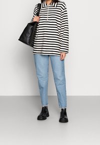 Schwarz-weiß gestreifter Pullover mit Reißverschluss-Kragen, hellblaue gerade Jeans mit fransigen Säumen und schwarze Stiefeletten. Schwarze Tote-Tasche.