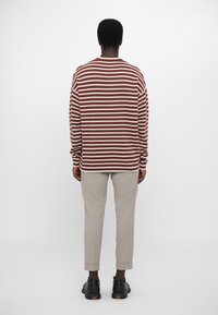 Braun-weißer gestreifter Pullover in entspannter Passform, gestrickte Textur, Rundhalsausschnitt und lange Ärmel. Kombiniert mit hellgrauen, schmal zulaufenden Hosen.
