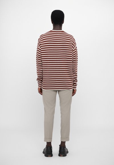 Suéter de rayas marrón y blanco con un corte relajado, textura de punto, cuello redondo y mangas largas. Combinado con pantalones ajustados gris claro.