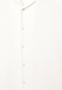 White, textured shirt with a vertical button placket, featuring five light-colored buttons and a soft, relaxed collar design.