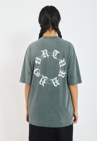 Grå oversized bomulds t-shirt med korte ærmer, prydet med et stort hvidt grafisk design på ryggen. Blød tekstur, afslappet pasform.