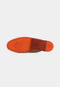 Semelle de chaussure en cuir orange vif avec armoiries en relief et marquages de la marque, montrant des coutures détaillées et un bord supérieur texturé.