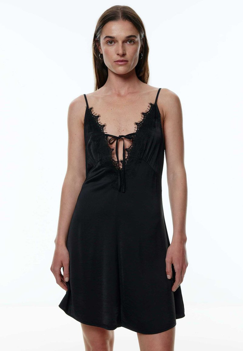 Schlafkleid aus schwarzem Satin mit Spitzenborte und tiefem V-Ausschnitt. Mit verstellbaren Trägern und einer Bindung vorne für eine figurbetonte Passform.