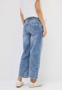 Vaqueros de mezclilla azul claro con un corte relajado, con un lavado desgastado, diseño clásico de cinco bolsillos y dobladillos remangados. Combinados con zapatillas blancas.