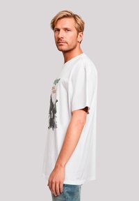 White cotton t-shirt with a relaxed fit, featuring a graphic design of a bear and trees in green and brown tones on the front.