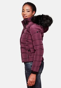 Maroon puffer jacket with a detachable black fur-lined hood, zip front, ribbed cuffs, and quilted texture. Paired with dark denim jeans.