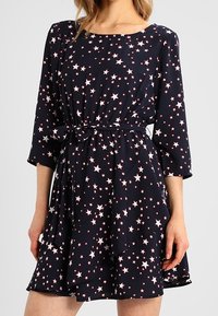 Marinblå klänning med rosa stjärnmönster, långa ärmar, midjesnörning och utsvängd nederkant. Tillverkad av mjukt tyg, lättviktig och med en flödande design.