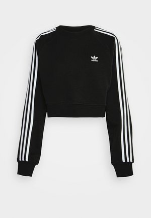 Fekete, rövidített pulóver hosszú ujjakkal, fehér háromsávos mintával a karok mentén, és kicsi hímzett logóval a mellrészen. Puha anyagból készült.