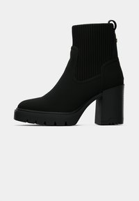 Crne gležnjače s rebrastim gornjim dijelom, debelim blok-štiklom i teksturiranom potplatom s utorima za prianjanje. Glatki materijal s čistim linijama.