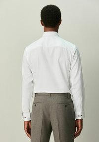 Bela srajca z dolgimi rokavi z teksturiranim vzorcem, s čisto ovratnico in manšetami na gumbe, kombinirana s sivimi hlačami po meri.