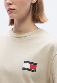 Μπεζ βαμβακερό t-shirt με τυπωμένο ορθογώνιο λογότυπο σε ναυτικό μπλε, λε υκό και κόκκινο. Σχέδιο με κοντά μανίκια και στρογγυλή λαιμόκοψη, με λεία υφή.