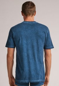 Blaues kurzärmliges Hemd aus weichem Material, mit leicht strukturierter Textur und Rundhalsausschnitt. Die Rückansicht zeigt eine einfarbige Gestaltung ohne Muster.