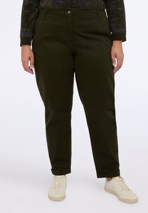 Personne portant un pantalon droit vert foncé avec des ourlets retroussés, associé à des baskets écrues et un haut à manches longues foncé.