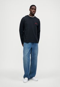 Cămașă neagră cu mâneci lungi, cu bordură albă la guler și logo roșu. Asortată cu blugi albaștri largi și adidași albi, creând o ținută casual.