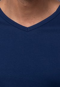 Granatowa koszulka z dekoltem w serek, wykonana z gładkiego materiału, charakteryzująca się prostym designem, eleganckim, dopasowanym krojem oraz minimalnymi detalami szwów.