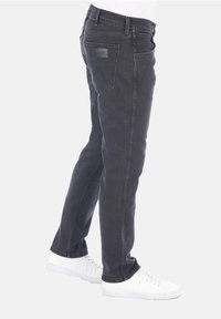 Černé džíny z denimu se střihem do rovna, s zadními kapsami a koženou nášivkou s logem značky. Nošeny s bílými teniskami.