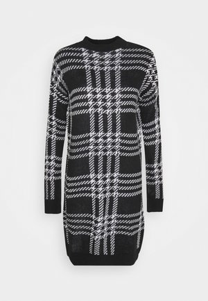 Czarna i biała sukienka swetrowa z długim rękawem, z dużym wzorem w kratę oraz ściągaczami u mankietów i na dole.