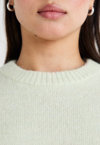 Lys grønn strikket genser med ribbestrikket rund hals. Myk tekstur med subtile vertikale linjer. Enkelt og minimalistisk design.