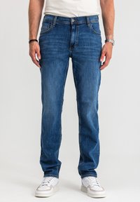 Niebieskie jeansy z denimu o klasycznym, prostym kroju, wyposażone w pięć kieszeni, subtelne przeszycia i czyste wykończenie. Noszone z białymi trampkami.